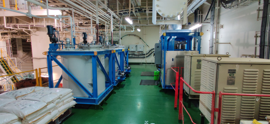 Industrial room with large blue machinery and beige equipment on a green floor.